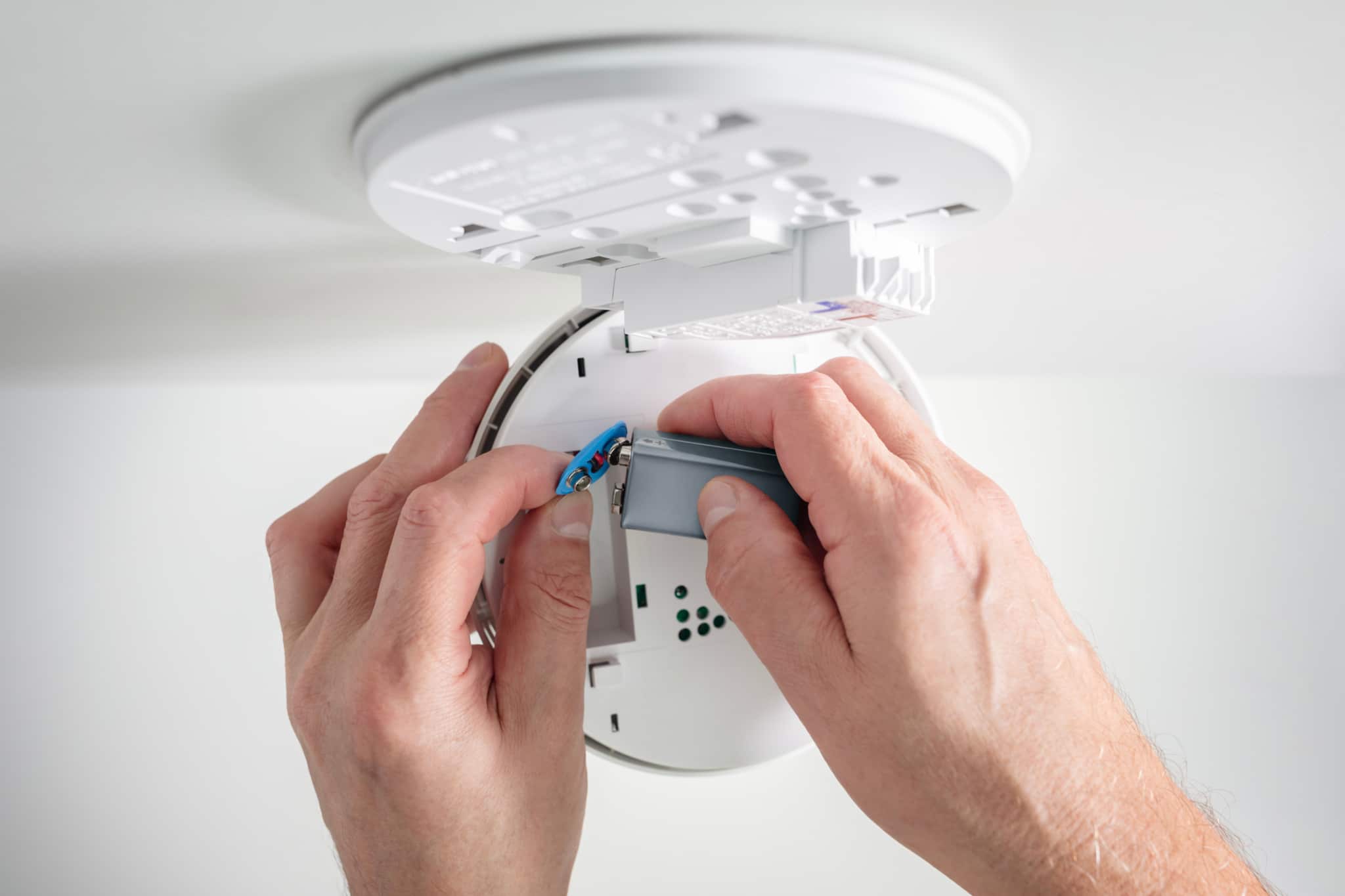 Replacing smoke detector battery for fire alarm system maintenance.